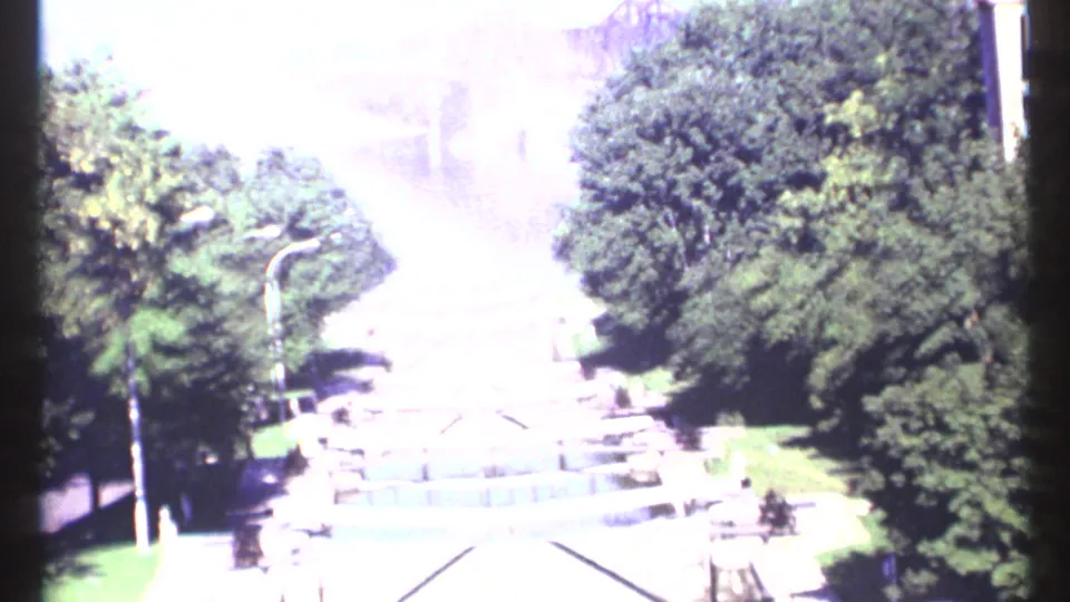 1967 Ottawa 8mm frame looking down over a tree-lined lakefront approach with steps and paths, heavily brightened by exposure shift.