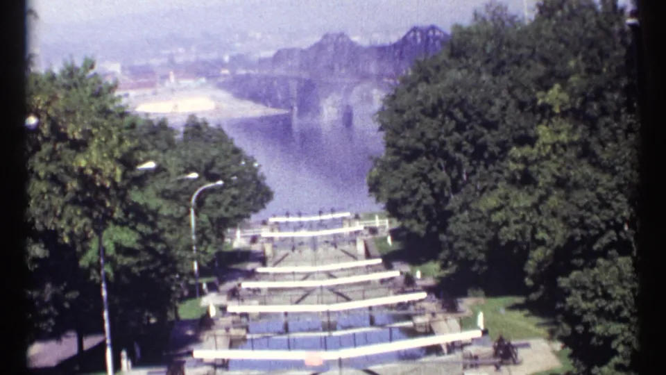 1967 Ottawa home-movie view over a broad river, framed by trees, white stepped railings, and a distant bridge.