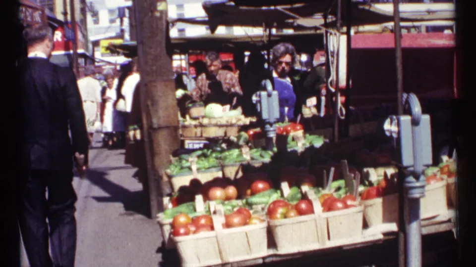 1967 Ottawa market sidewalk with shoppers near a produce stand as a suited man walks beside baskets of vegetables.