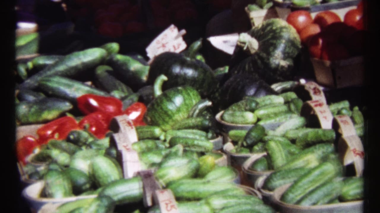 Produce stand with cucumbers, squash, red vegetables, baskets, and small price cards.
