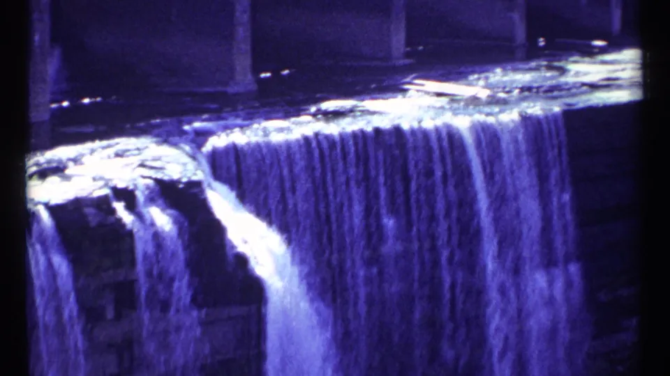 1967 Ottawa home-movie frame showing a blue-purple tinted waterfall cascading over stepped stone ledges.
