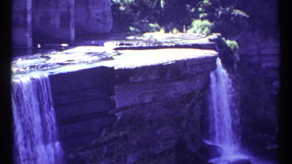 1967 Ottawa frame of water falling from a constructed rocky ledge, with foliage visible above the structure.
