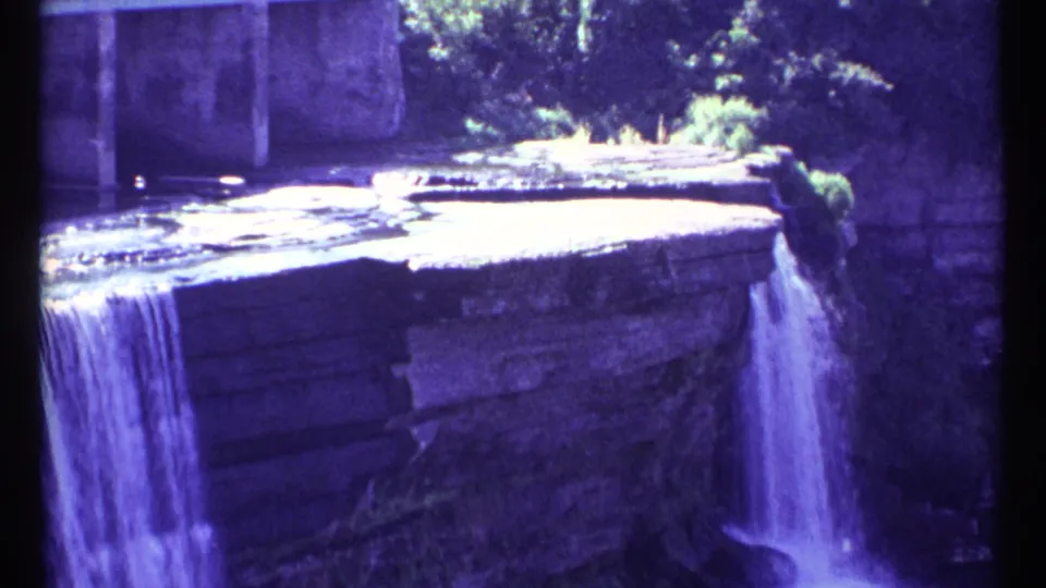 Blue-purple 8mm frame from Ottawa showing a waterfall spilling over a man-made stone edge into a lower area.