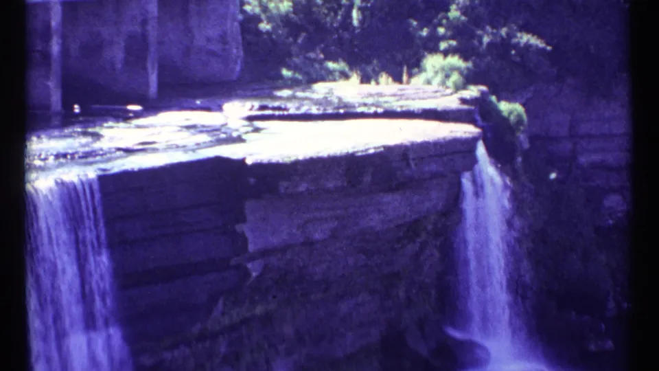 1967 Ottawa home-movie frame showing a narrow stream falling from a flat stone ledge with trees behind it.