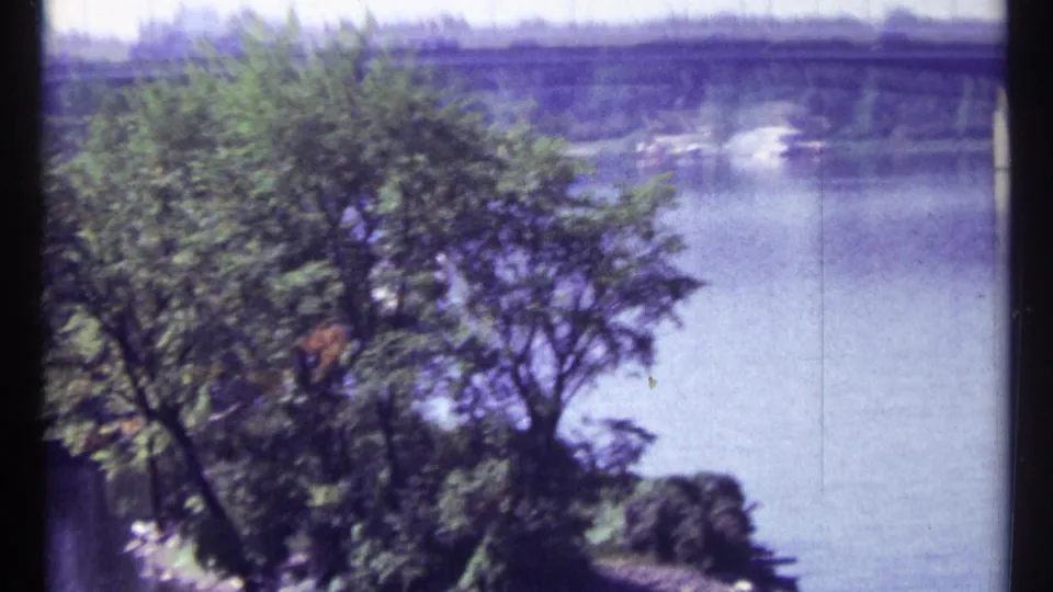 1967 Ottawa 8mm frame showing foreground trees, a wide river, and a distant concrete dam or bridge structure.