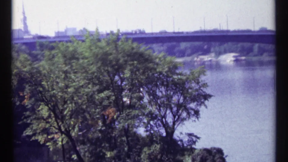 Ottawa riverfront view from 1967 8mm footage, with trees in the foreground and a distant dam or bridge-like span.