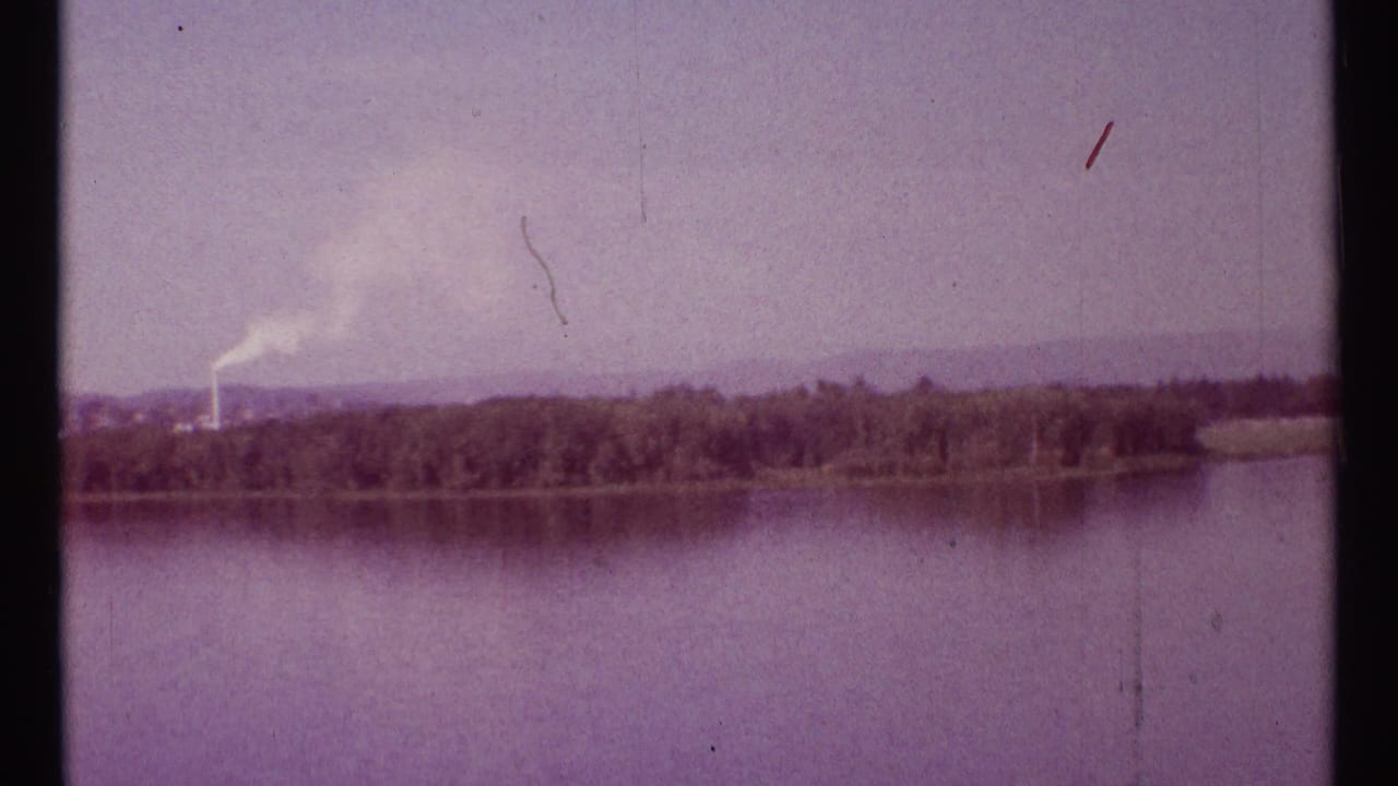 Wide river and far tree line with a smoke plume rising near the shore.