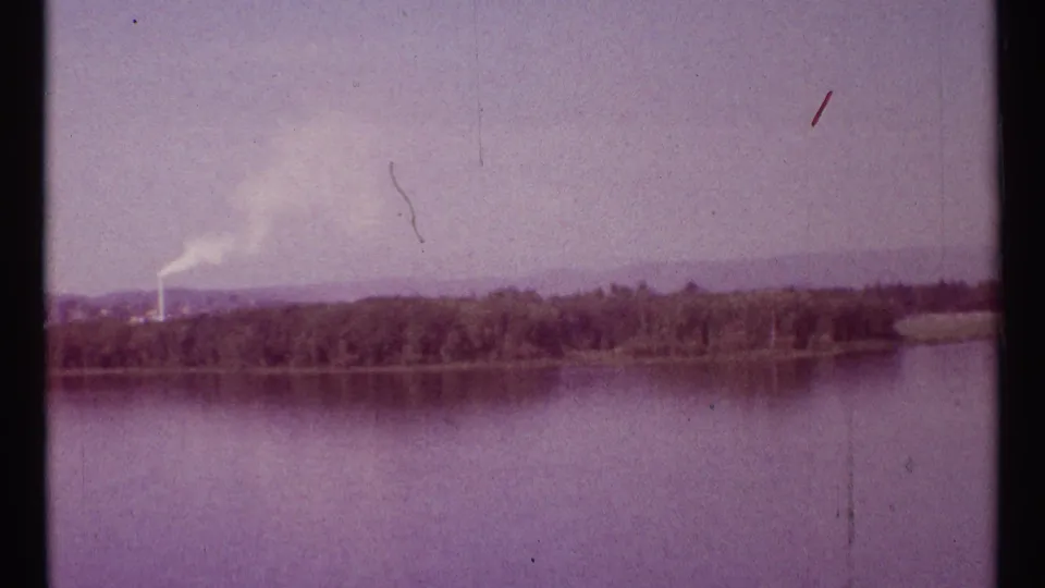 Ottawa River view with a wooded far bank and a factory chimney or stack emitting smoke in the distance.