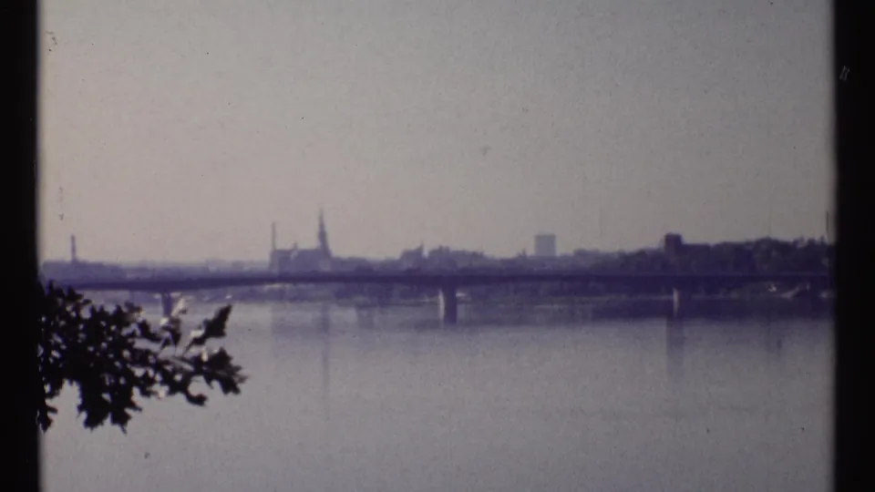 Ottawa River scene with calm water, a bridge span, distant buildings, and a prominent spire on the skyline.