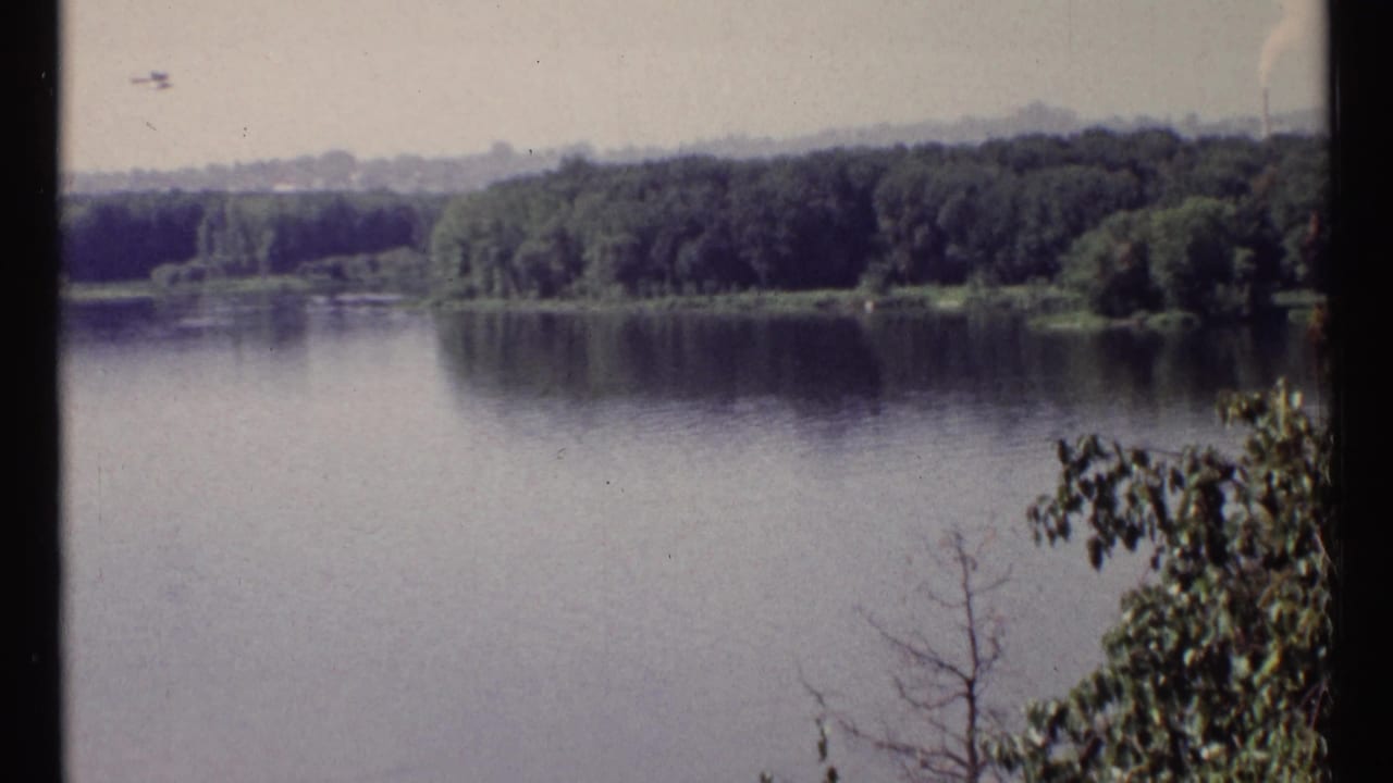 Calm river bordered by wooded shoreline under a hazy sky.