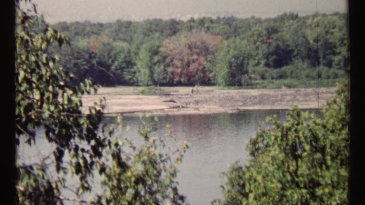 1967 8mm Ottawa-area river view with wooded banks, sandy shoreline, calm water, and leaves framing the scene.