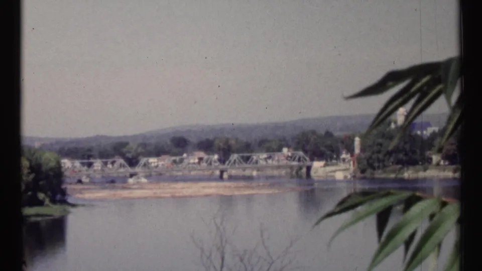 1967 Ottawa-area home-movie view of a river, metal truss bridge, sandy shoreline, trees, and low hills beyond.