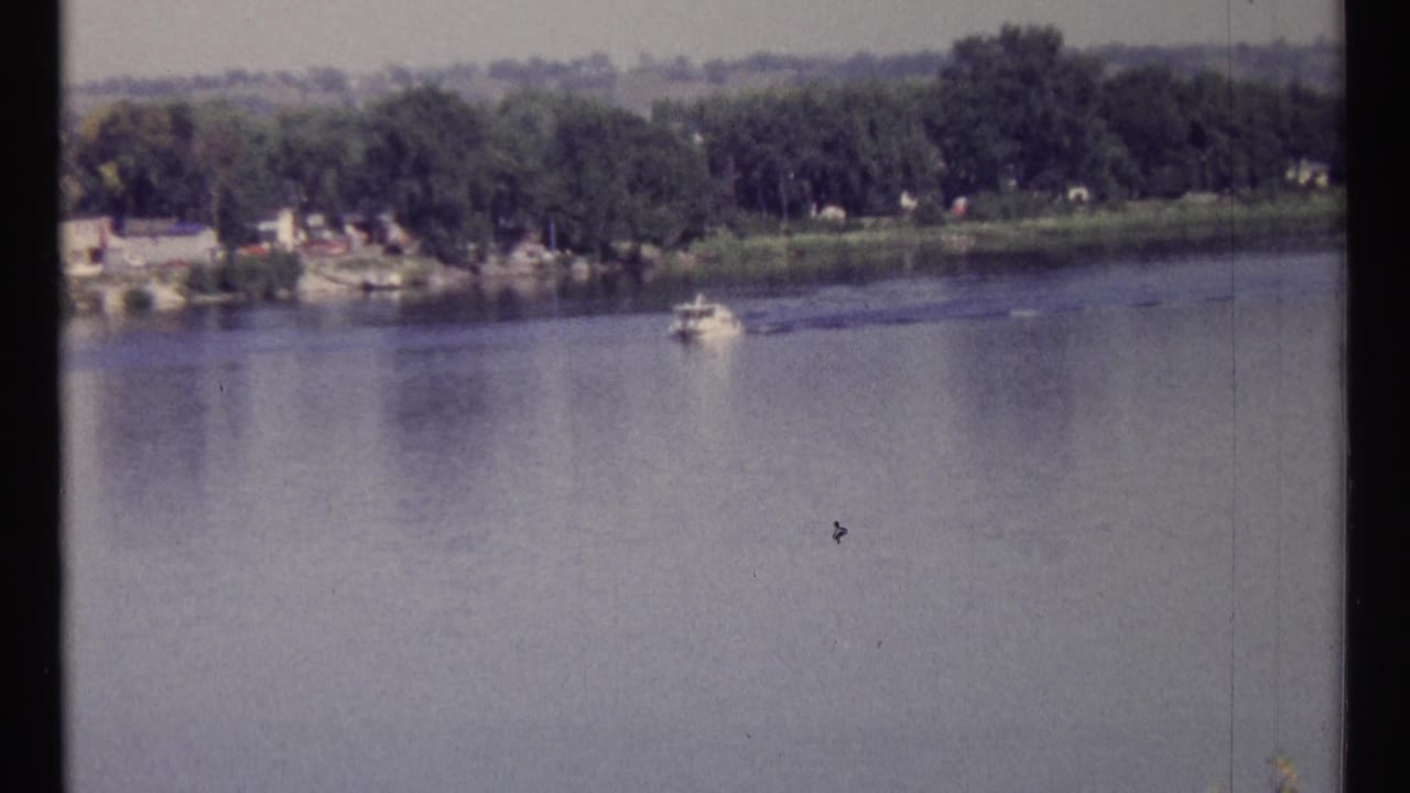 Small boat crossing a broad river with a wooded far shoreline.