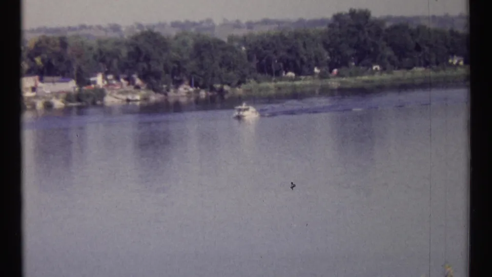 1967 Ottawa river view with a small boat moving across calm water and a wooded shoreline in the distance.