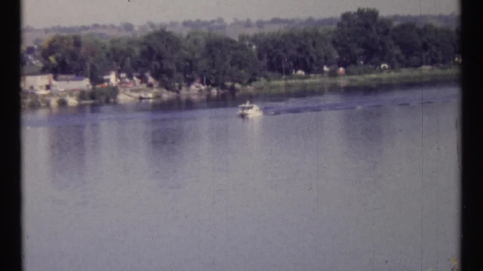 1967 Ottawa home-movie frame with a small boat on the river and a tree-covered far bank.