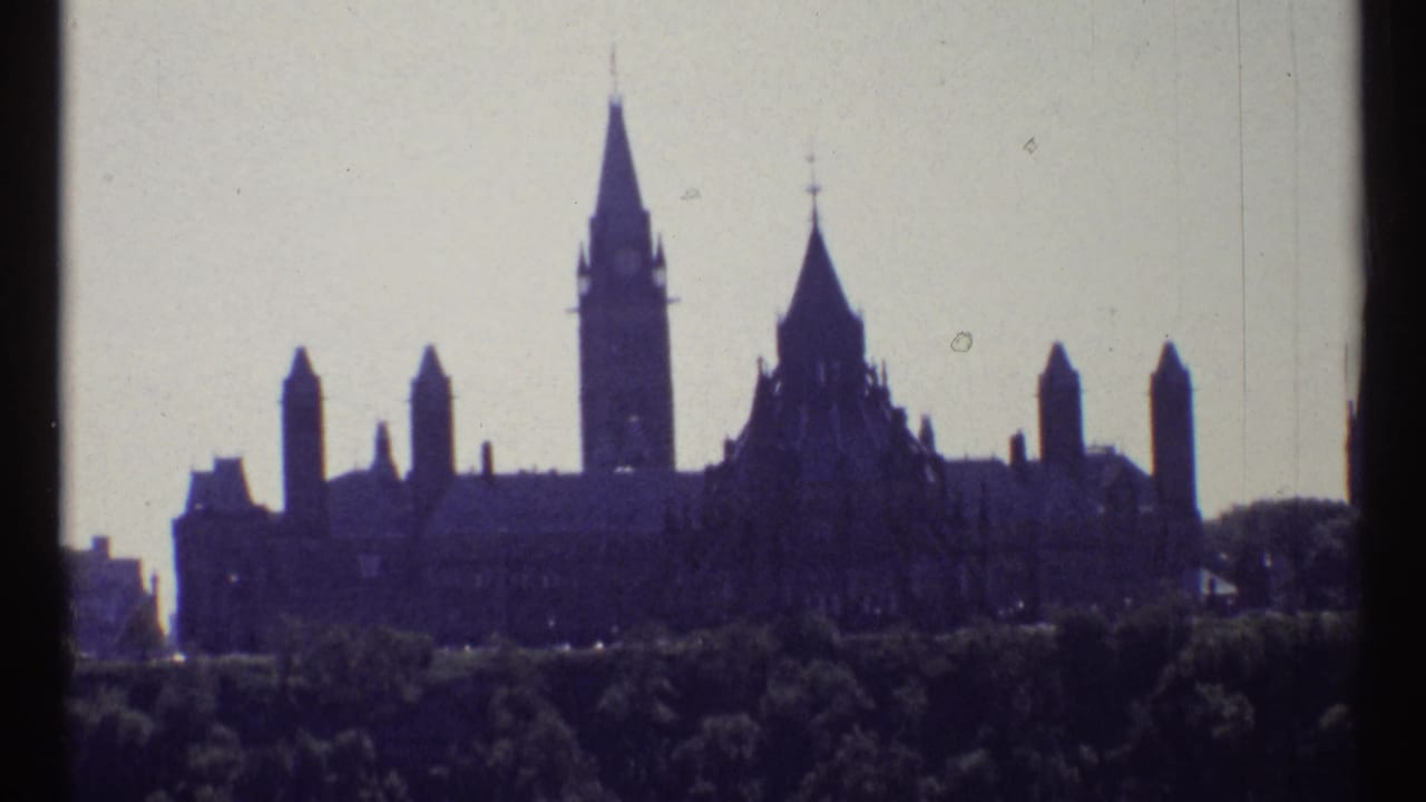 Distant Parliament skyline with central tower and pointed roofs above trees.