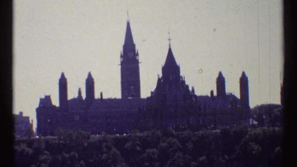 Ottawa Parliament skyline with the Peace Tower centered above a dark foreground of trees in soft 8mm color.