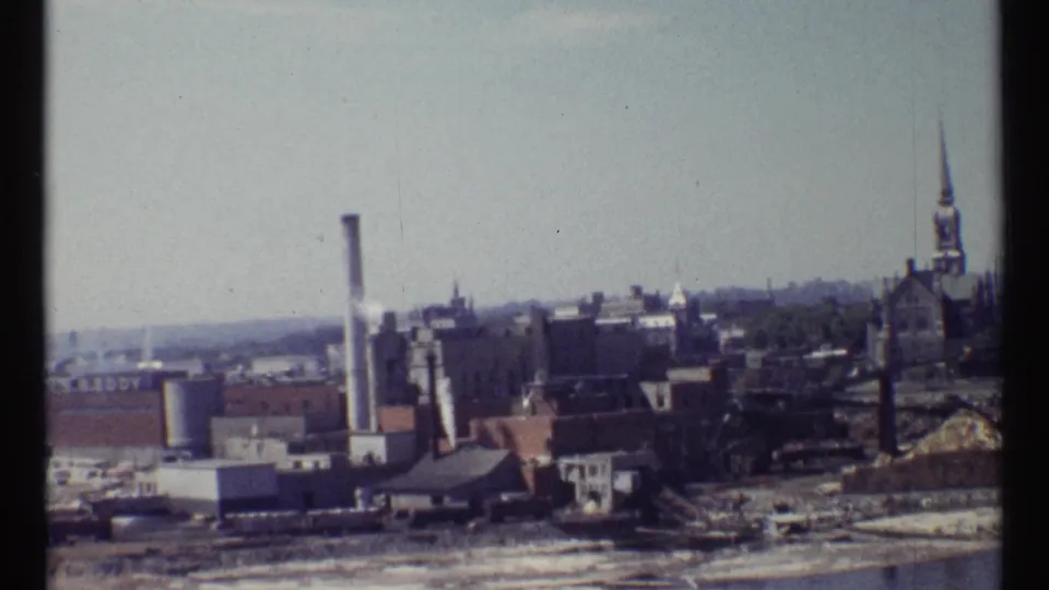 Ottawa city view on 8mm film showing industrial buildings, a tall smokestack, rooftops, and a church spire in the distance.