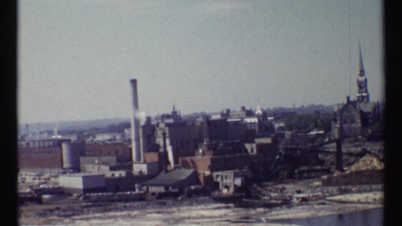 Elevated view of industrial buildings, a smokestack, and a church steeple in the distance.