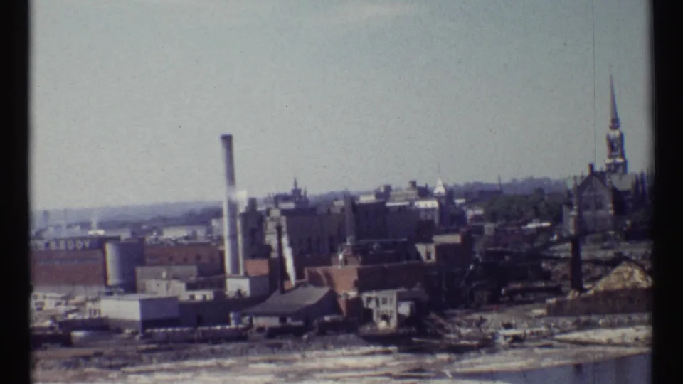 1967 Ottawa 8mm frame showing an industrial district with a smoking stack and church steeple beyond brick buildings.