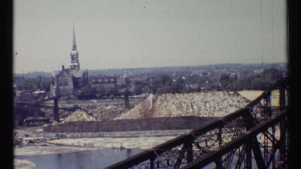 Ottawa 8mm view showing a dark metal bridge, pale gravel or rubble pile, industrial yard, and distant church steeple.