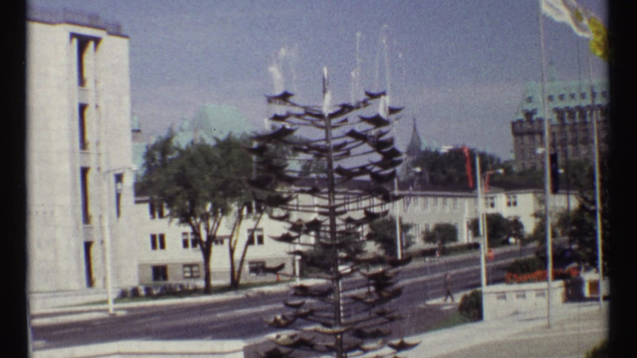 Civic street scene with metal sculpture, white buildings, flagpoles, and distant cars.