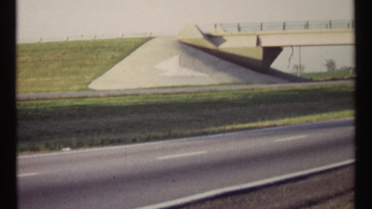 A concrete overpass and sloped embankment stand beside a highway with blurred traffic lanes.