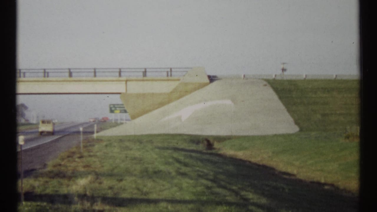 Highway overpass with a white arrow painted on a sloped grassy embankment.
