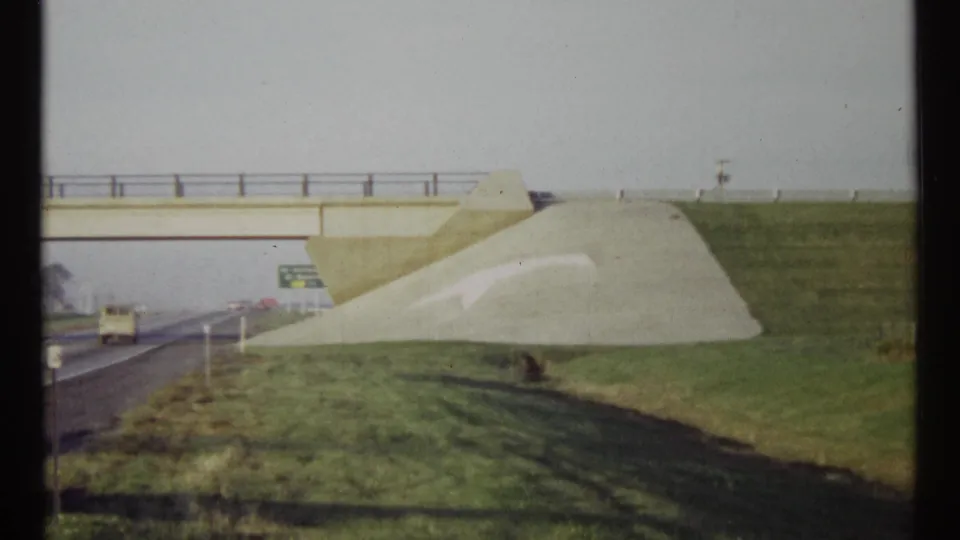 Ottawa highway scene from 1967 showing an overpass, road below, green fields, and a large white directional arrow on the slope.