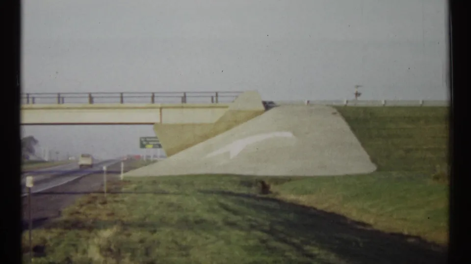 Ottawa highway cutaway from 1967 with a concrete overpass, green field, painted embankment arrow, and distant road traffic.