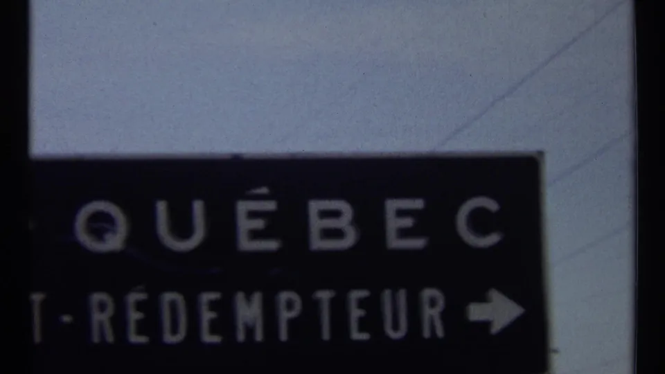 1967 Ottawa-area 8mm frame showing a dark directional sign with Québec lettering, partial St-Rédempteur text, and a right arrow.