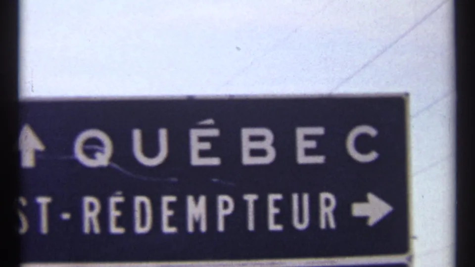 1967 Ottawa-area 8mm frame showing the Québec directional sign cropped low, with partial St-Rédempteur lettering and arrows.