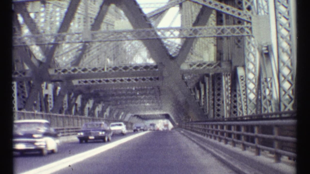 Forward view across a steel truss bridge with oncoming classic cars.