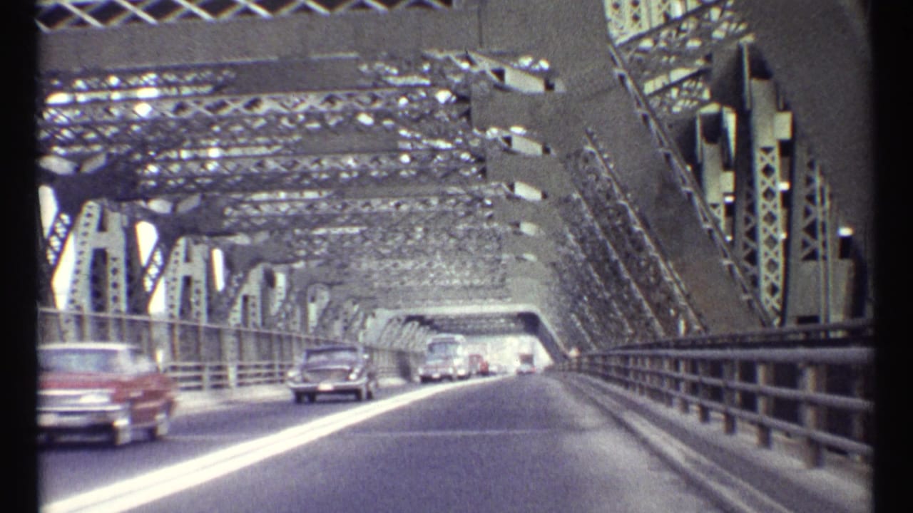 Cars travel along a roadway inside a large steel truss bridge.