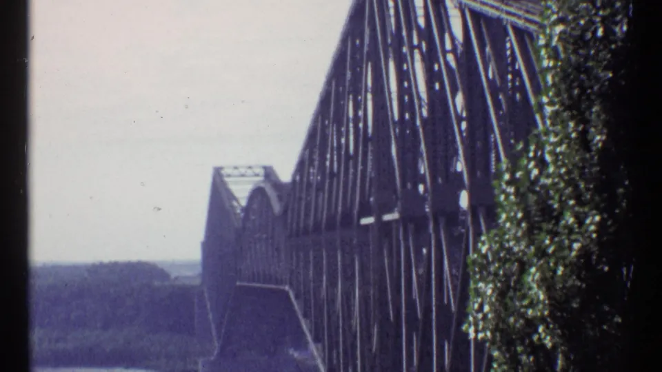 1967 Ottawa frame of Alexandra Bridge, showing repeating steel members, a stone pier, trees, and hazy river distance.