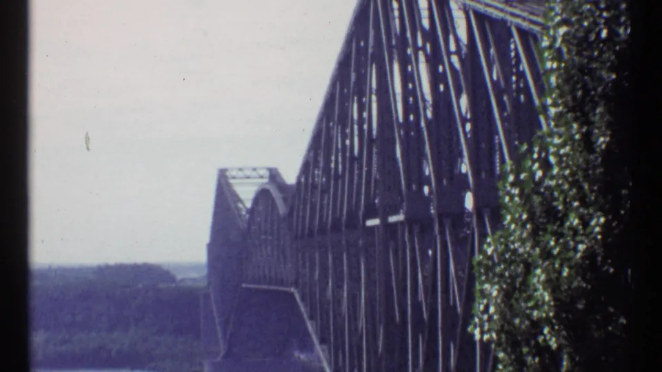 1967 Ottawa 8mm still of Alexandra Bridge seen close to the truss, with foliage, pale sky, and distant river landscape.