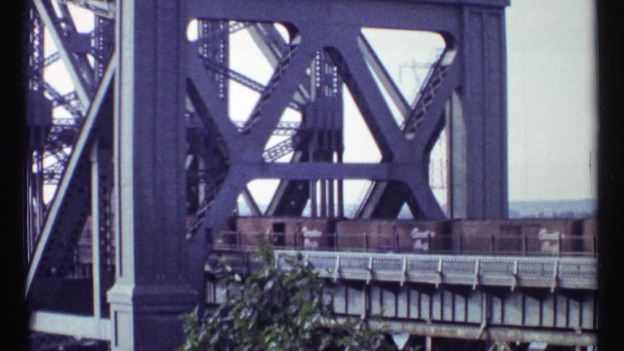 Brown freight cars on a steel bridge framed by large dark truss members.