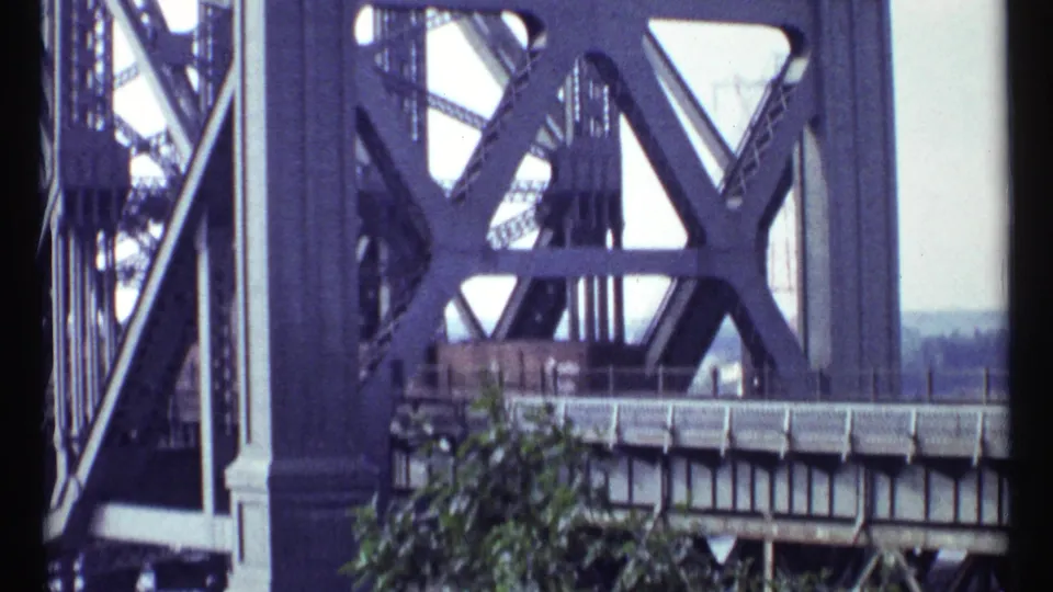 1967 Ottawa home-movie frame showing a large steel truss bridge with trees and distant landscape beyond it.