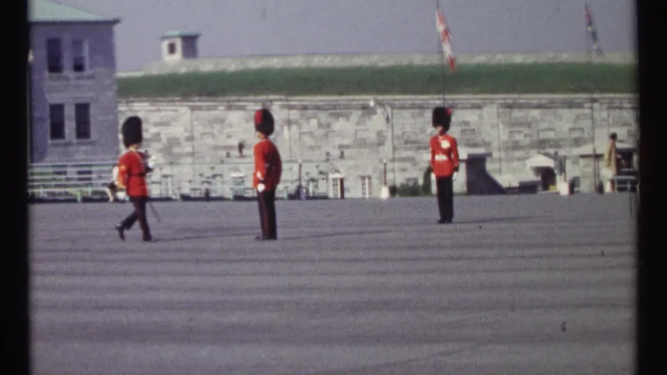 1967 Ottawa frame showing ceremonial guards crossing and standing on an open parade ground with a Canadian flag behind them.