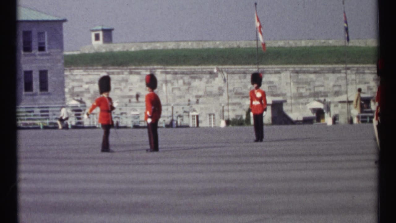 Three red-uniformed guards stand on a wide courtyard before stone walls and flags.