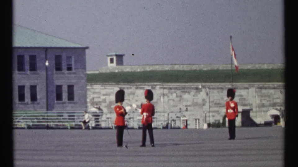 Home-movie frame of two ceremonial guards grouped near the center and a third guard standing apart on the Ottawa parade ground.