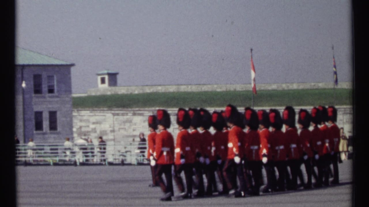 A formation of guards in red tunics marches across a wide parade ground.