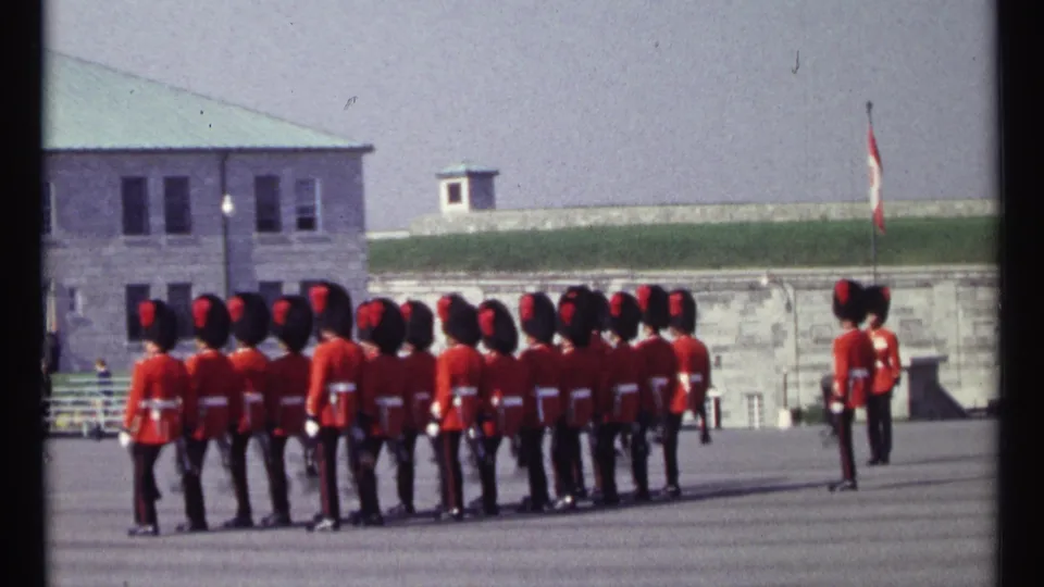 Canadian guards continue their ceremonial march in a 1967 Ottawa home-movie frame, with another guard standing to the side.