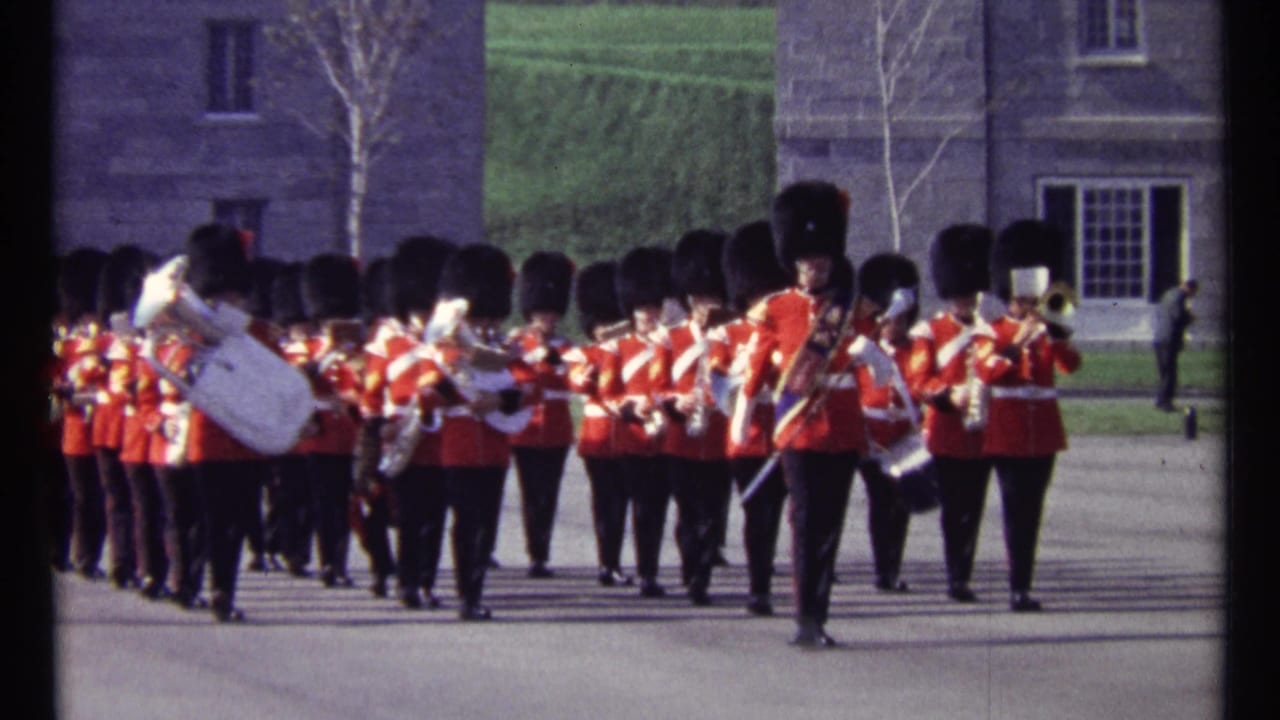 1967 Ottawa home-movie frame showing a red-uniformed military band marching with brass instruments near stone buildings.