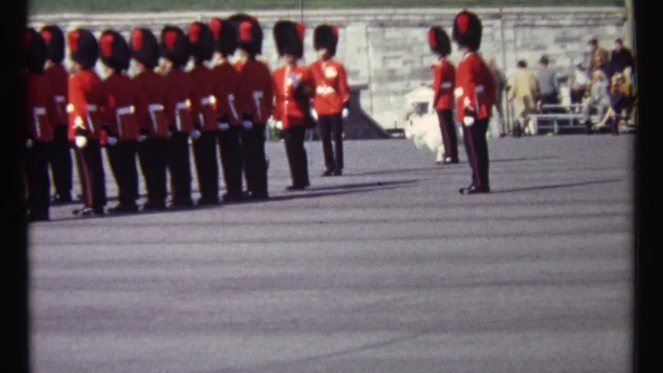 Ottawa 1967 home-movie frame of a ceremonial band lined up on a paved ground, with spectators near the stone wall behind.