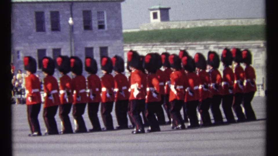 1967 Ottawa home-movie frame showing ceremonial guards marching in formation past stone buildings and a parade ground.