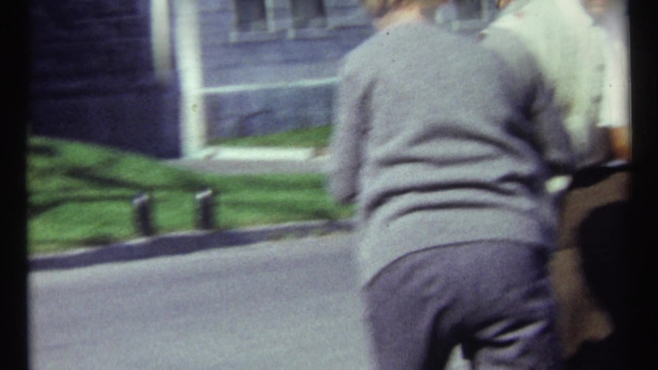 Blurry street view with a bystander in front of stone buildings and lawn.