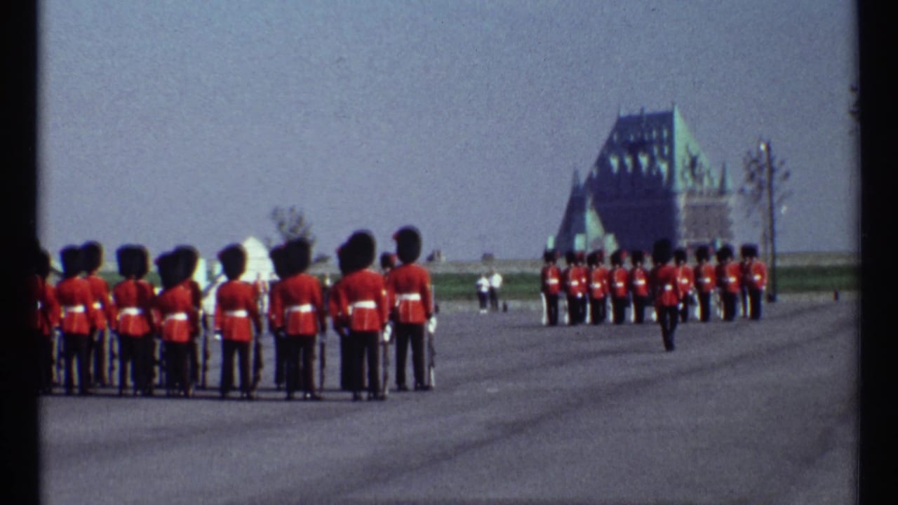 Rows of red-coated guards stand in formation on a broad paved area.