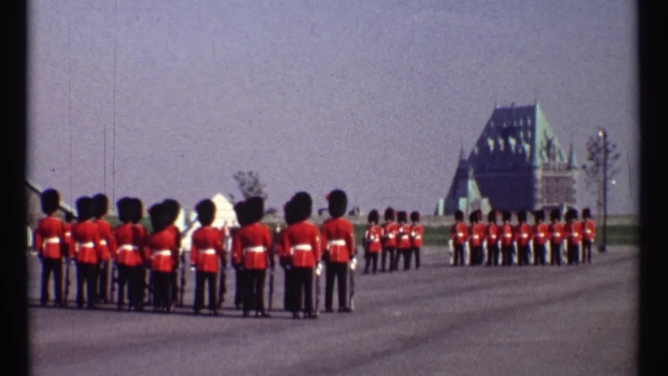 1967 Ottawa footage frame with red-coated guards seen from behind and additional ceremonial soldiers arranged farther down the paved ground.