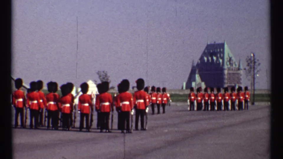 Ottawa ceremonial parade frame showing guards in red tunics and bearskin hats from a home-movie viewpoint, with formal buildings beyond.